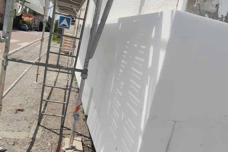 Échafaudage et panneaux de polystyrène en cours de pose sur la façade, chantier d'isolation par l'extérieur