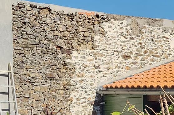 Vue rapprochée du mur en pierre, partie rejointoyée et partie d'origine, deux ouvriers au travail