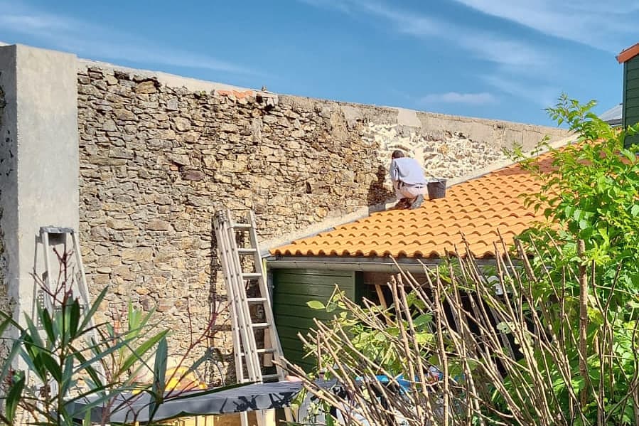 Mur en pierre en cours de reprise des joints, échelles et bâches de chantier au pied